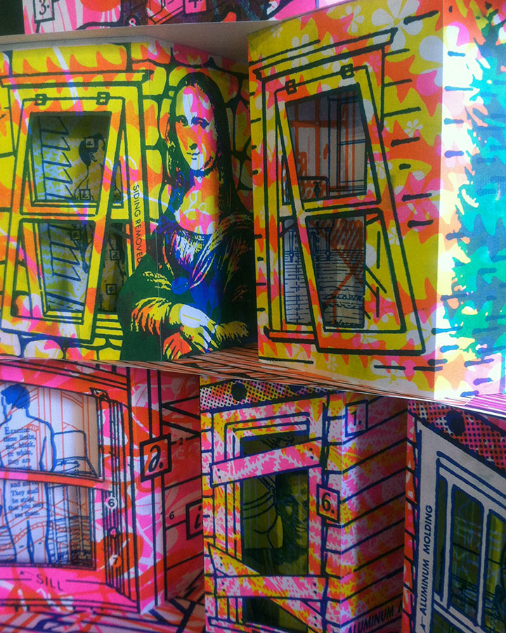 Close up photo of a paper sculpture arranged like an apartment building. The windows are cut out of the paper, and an inner layer with illustrations of nude or partially nude men are visible. 