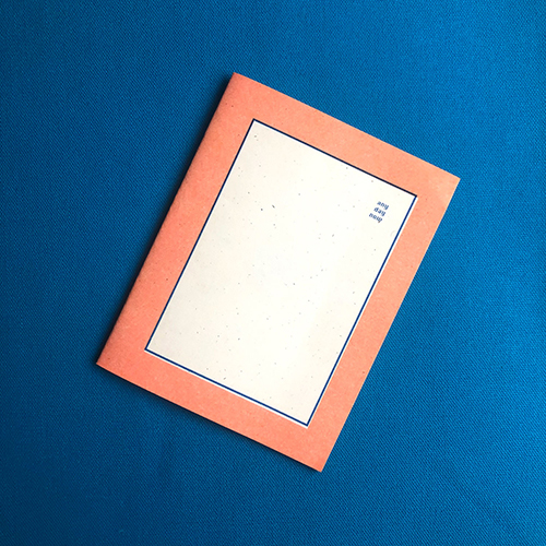 Photograph of a small zine with an orange border, blue lined with a blank center. 