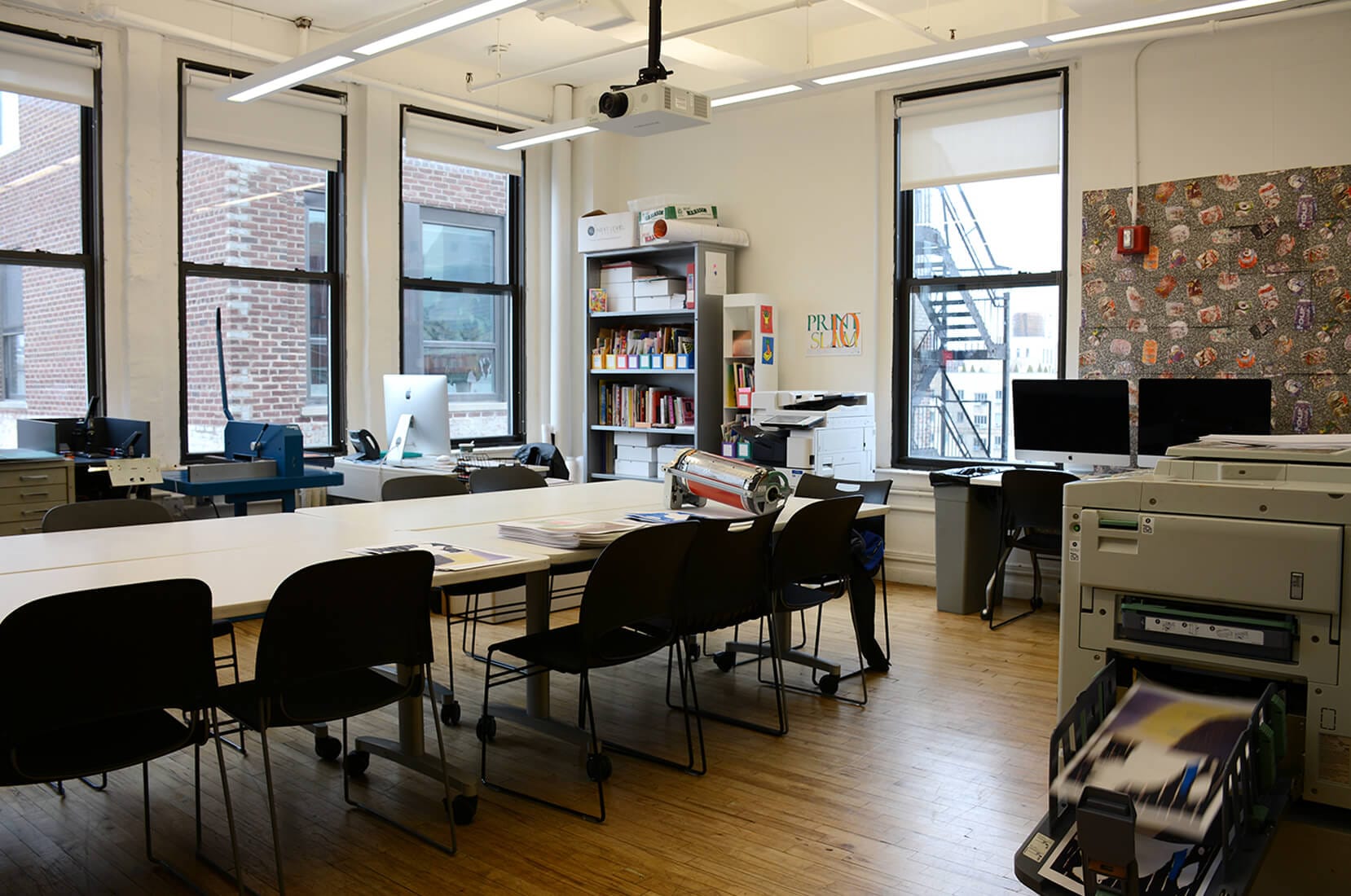 A photo of the Risolab as seen from the main entrance, showing one of the Risograph printers and the central table where students sit.