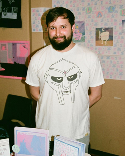 Photograph of Alex laird, who has dark hair and a beard, and wears a graphic t-shirt.