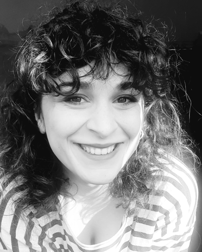 Black and white photograph of Khatia Chitorelidze smiling, she has curly dark hair and wears a striped shirt.