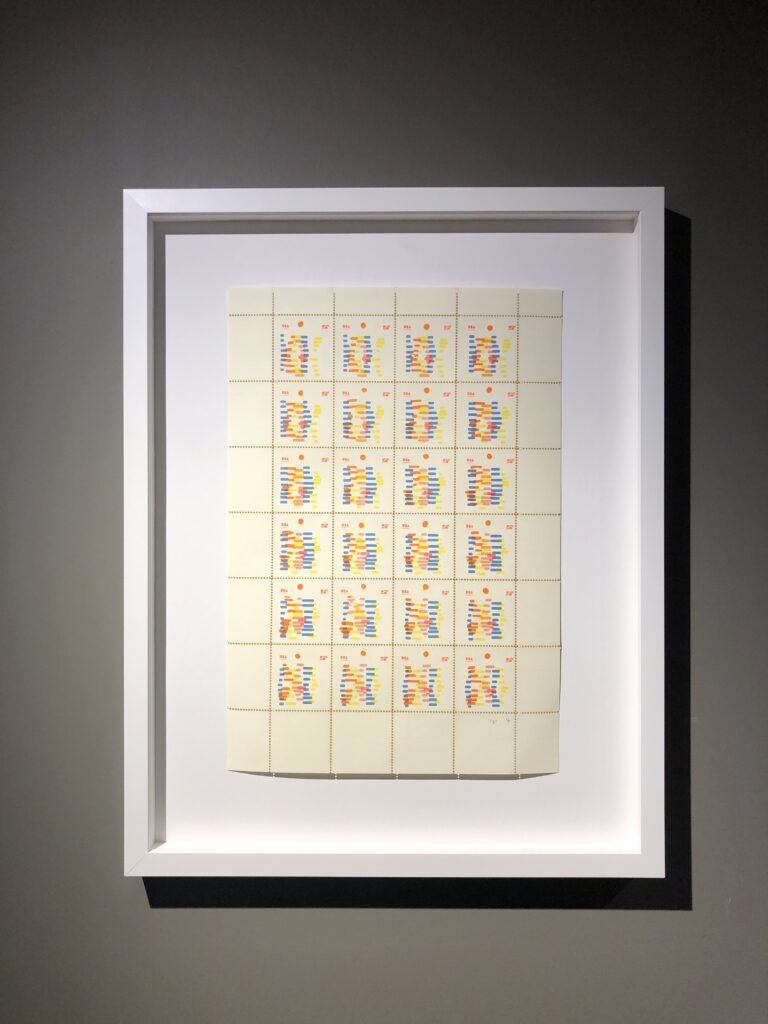Photo of a framed riso print, abstract shapes in orange, yellow, pink and blue repeated in a grid format.