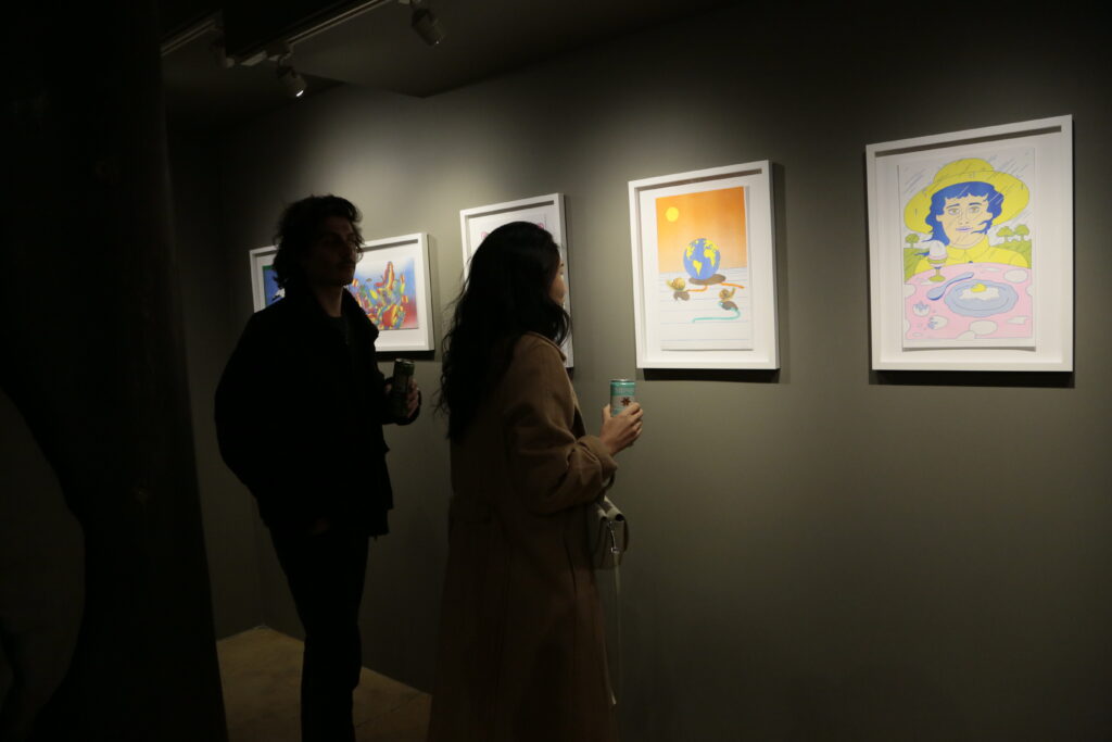 Photo of opening night at "Printing the Future" exhibition. Two people look at framed riso prints against a wall.