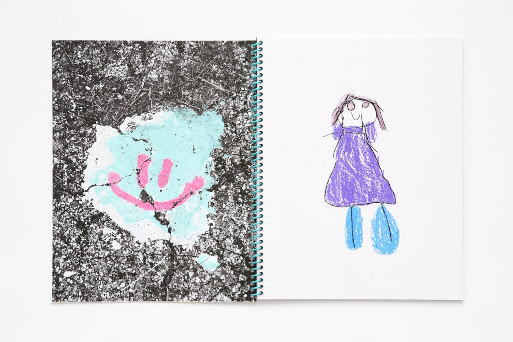 Double page spread, left page is a photograph of gravel and dirt with an aqua and pink smiley face painted on it, right page is a child's drawing of a figure in a purple dress and blue shoes.
