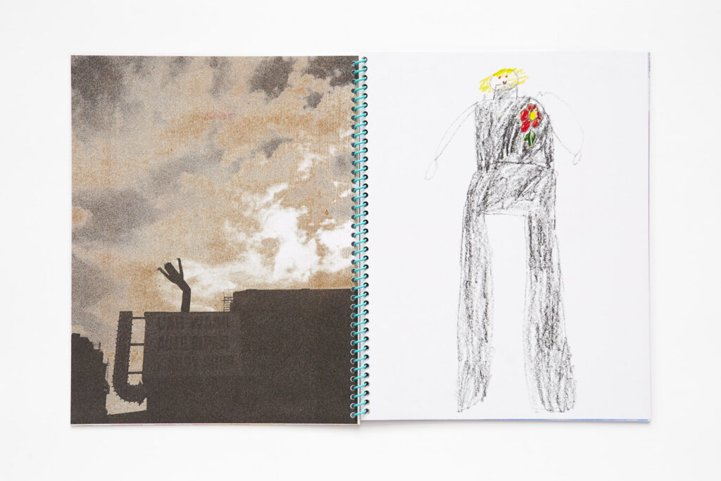 Double page spread, left page is a black and gold duotone photo of the silhouette of buildings and a wacky inflatable man against a cloudy sky, the right page is a child's drawing of a figure with yellow hair, wearing black and a red flower on their chest.