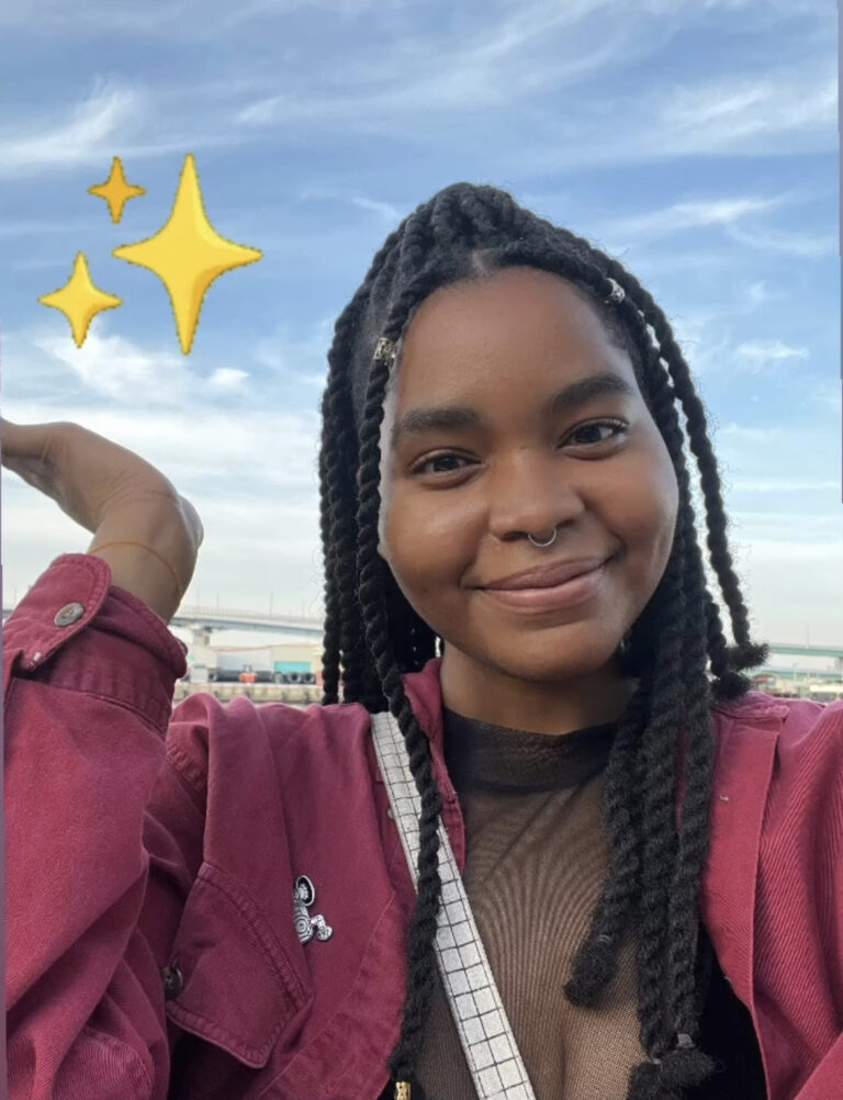 Smiling girl with braids wearing a red shirt holding up her hand, Sabi Borno