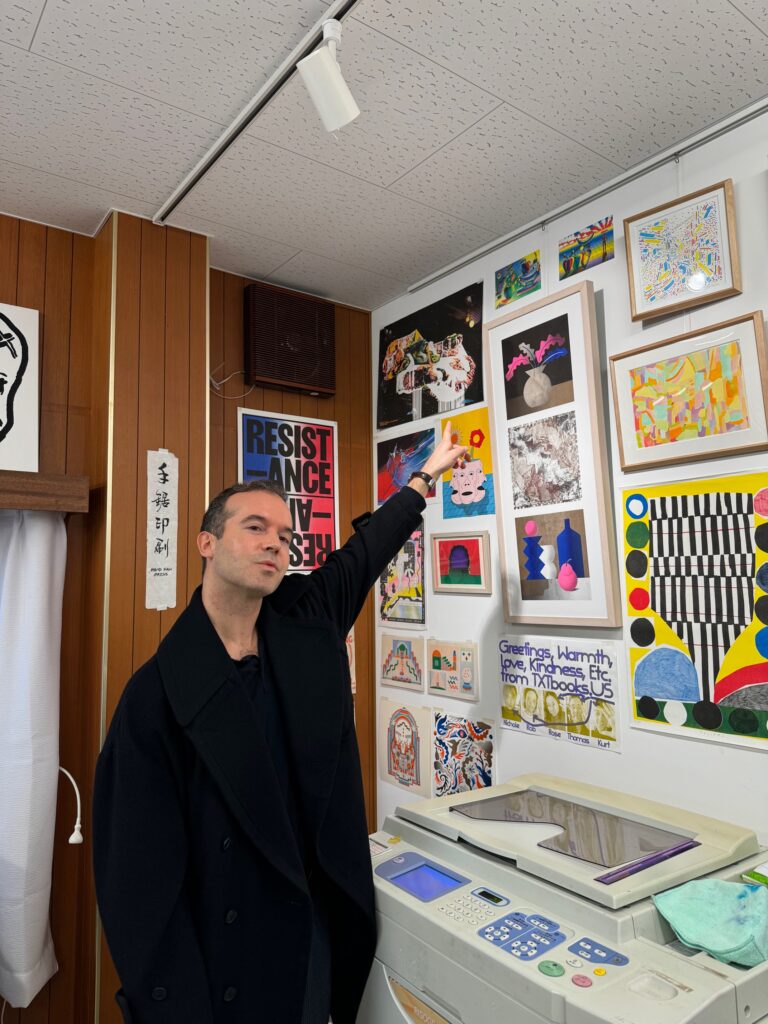 A man - Pan Terzis- pointing at his print on the wall with head tilted