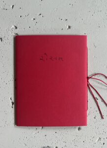 Cover of Sarah Hakani Zarina's publication, bound in red paper with red thread, the title, "Rosana" written in Gujarati, 'રોસન.'