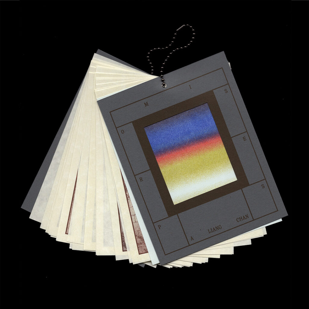 A book bound by one hole in the top, the cover is gray with a cut out square of primary color gradients.