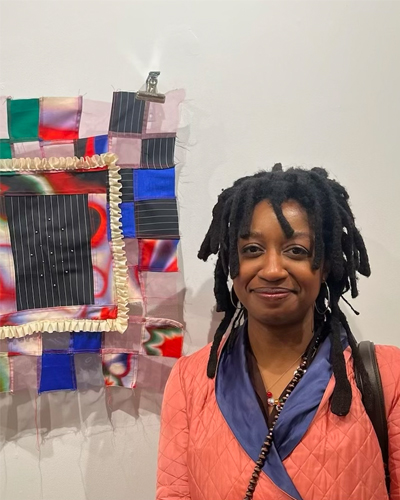 Headshot of AIR Mia, a Black woman with locs, smiling and wearing a blue shirt and pink sweater.
