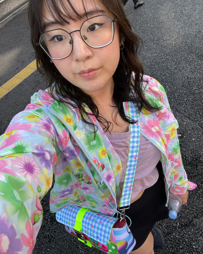 Picture of Jackie Liu, who has dark wavy hair, glasses, and wears bright pastel colors.